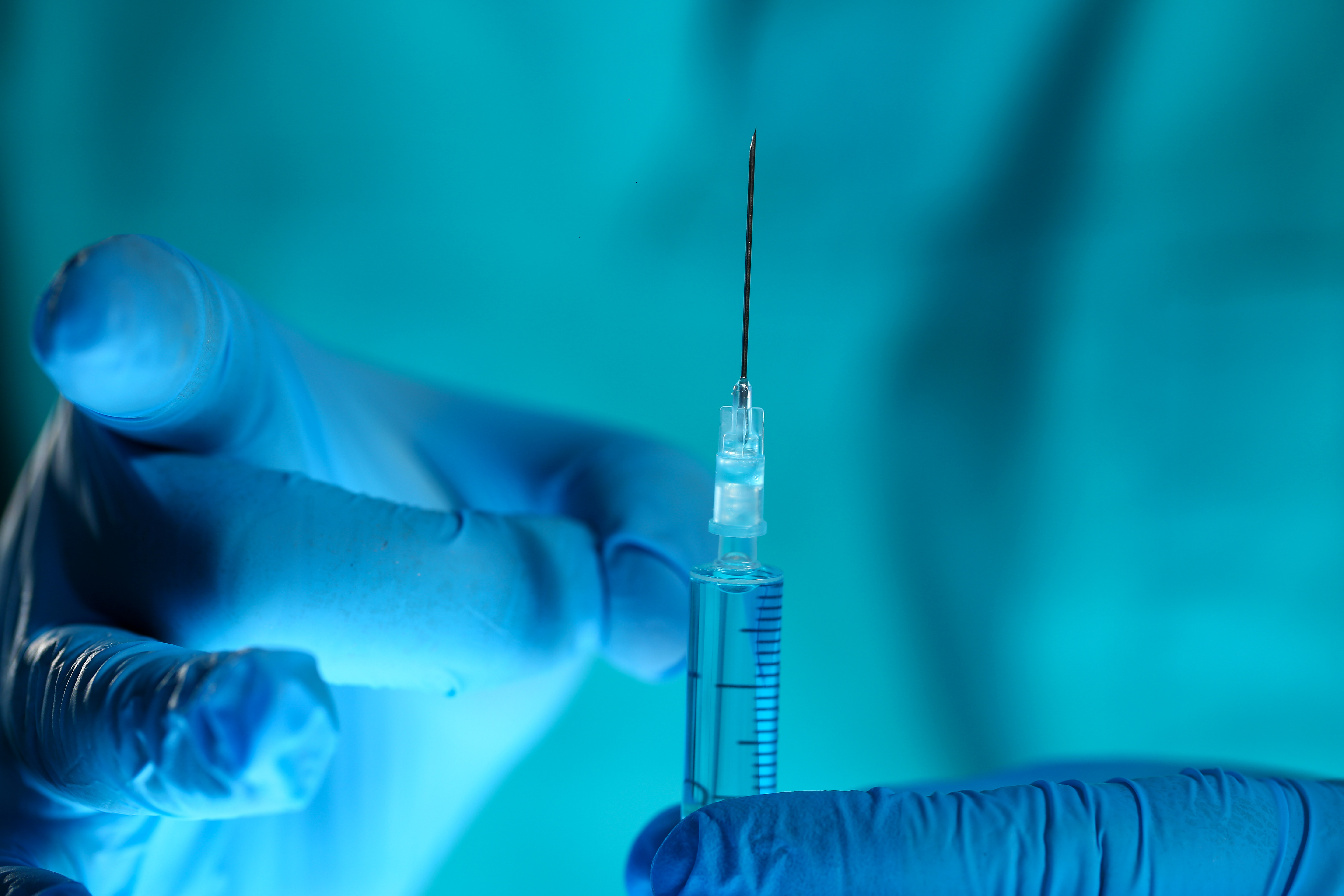 laboratory scientist holds and flicks a thin-needled syringe with blue-gloved hands